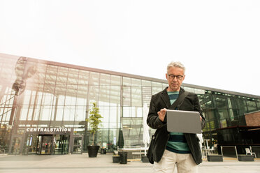Älterer männlicher Pendler mit digitalem Tablet vor dem Bahnhofsgebäude - MASF08521