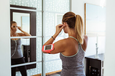 Frau in Sportkleidung mit Kopfhörern beim Blick in den Spiegel zu Hause - MASF08542