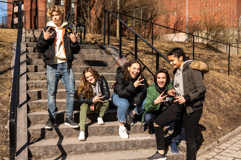 Fröhliche multiethnische Teenagerfreunde gestikulieren auf einer Treppe in der Stadt, lizenzfreies Stockfoto