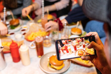 Abgeschnittenes Bild eines Teenagers, der Essen und Getränke auf dem Tisch eines Restaurants fotografiert - MASF08564