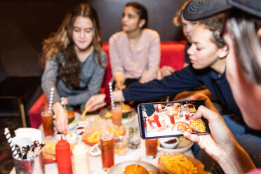 Cropped image of teenage boy sitting with friends while photographing food and drinks on table at restaurant - MASF08565
