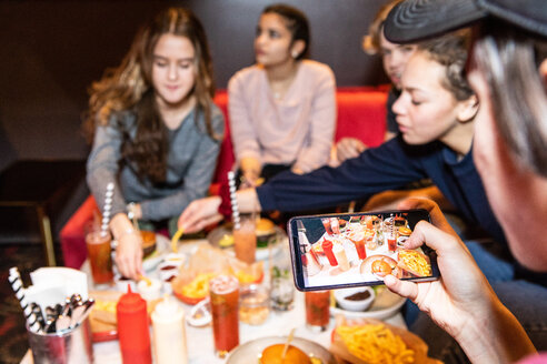 Ausgeschnittenes Bild eines Teenagers, der mit Freunden zusammensitzt und Essen und Getränke auf dem Tisch eines Restaurants fotografiert - MASF08565