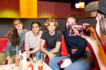 Ausgeschnittenes Bild eines Teenagers, der seine multiethnischen Freunde fotografiert, die in einem Restaurant auf dem Sofa sitzen - MASF08566