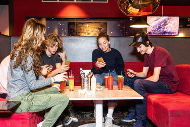 Multiethnische Freunde im Teenageralter benutzen ihr Smartphone, während sie mit Mocktails auf dem Sofa im Restaurant sitzen - MASF08569