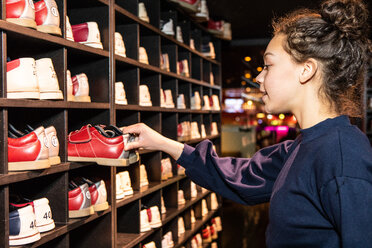 Seitenansicht eines jungen Mädchens, das Bowlingschuhe an einem Holzständer hält - MASF08574