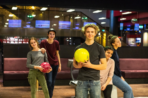 Porträt eines lächelnden Teenagers, der eine Kugel hält, während er auf einer Bowlingbahn gegen Freunde antritt, lizenzfreies Stockfoto