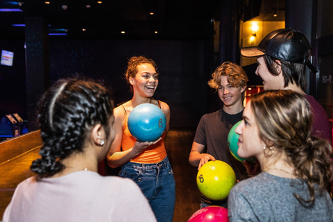 Fröhliche multiethnische Teenager unterhalten sich, während sie Bowlingkugeln halten, lizenzfreies Stockfoto