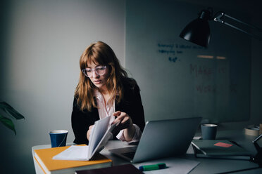 Confident young businesswoman reading document while sitting with laptop at creative office - MASF08594