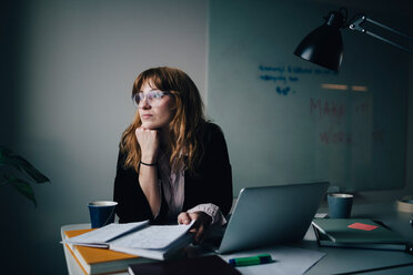 Thoughtful young businesswoman sitting with document and laptop at creative office - MASF08595