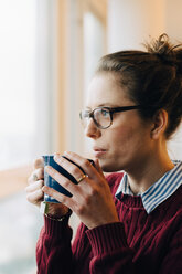 Nachdenkliche Geschäftsfrau, die Kaffee trinkt und durch ein Fenster auf ein kreatives Büro blickt - MASF08608