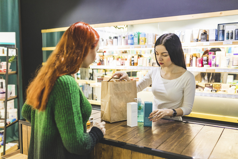 Verkäuferin und Kundin verpacken Produkte in einer Papiertüte in einem Kosmetikgeschäft, lizenzfreies Stockfoto