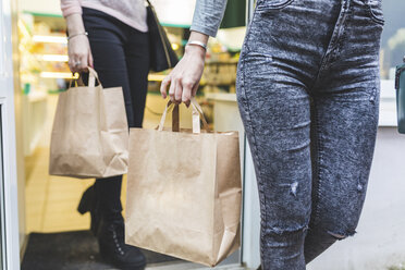 Close-up of two women leaving shop holding paper bags - WPEF00671