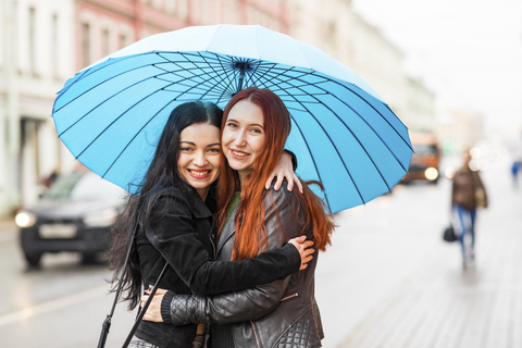 Zwei glückliche Frauen umarmen sich an einem regnerischen Tag in der Stadt, lizenzfreies Stockfoto