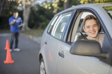Lächelnder Fahrschüler, der das Fahren lernt und in den Außenspiegel eines Autos schaut - ZEF15798