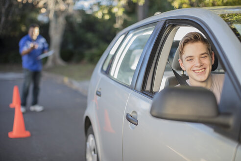 Smiling learner driver learning to drive looking at wing mirror of a car - ZEF15798