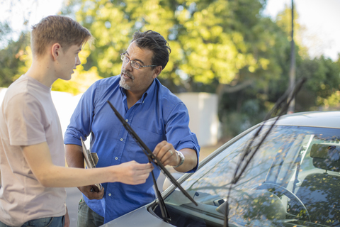 Learner driver with instructor checking windscreen wipers of a car stock photo