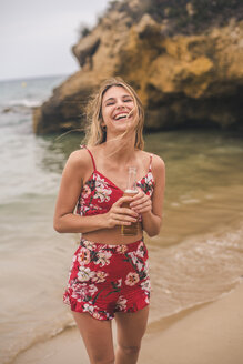 Portrait of happy young woman standing with a beer on the beach - ACPF00102