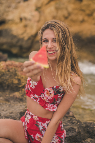 Portrait of happy young woman on rocks at the sea holding watermelon slice stock photo