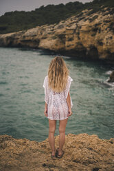 Rückansicht einer jungen Frau, die auf einem Felsen an der Küste steht - ACPF00111