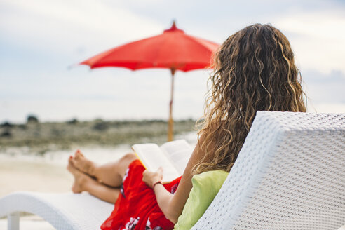 Thailand, Rückenansicht einer Frau, die am Strand ein Buch liest - MOMF00471