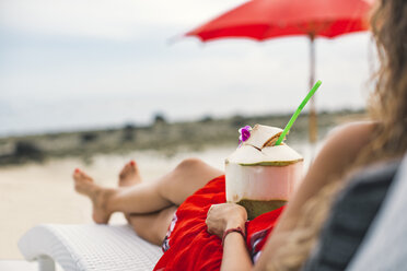 Thailand, Rückenansicht einer Frau auf einer Sonnenliege mit frischer Kokosnuss am Strand - MOMF00476