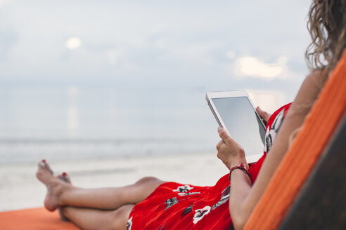 Thailand, Koh Phangan, Frau auf Sonnenliege sitzend mit digitalem Tablet am Strand - MOMF00480