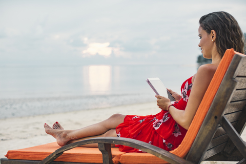 Thailand, Koh Phangan, woman sitting on sunlounger on the beach using digital tablet stock photo
