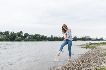 Smiling woman splashing water in a river - UUF14446