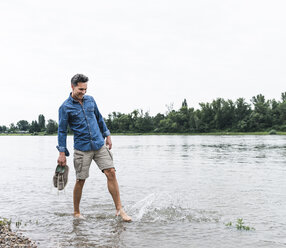 Lächelnder Mann spritzt Wasser in einem Fluss - UUF14462