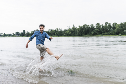 Lachender Mann, der in einem Fluss Wasser spritzt, lizenzfreies Stockfoto