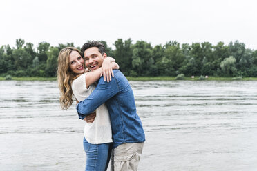 Porträt eines glücklichen Paares, das sich am Flussufer umarmt - UUF14477