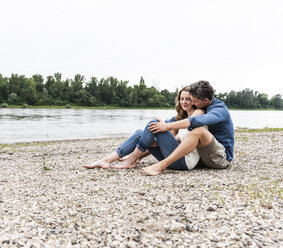 Affectionate couple sitting at the riverside - UUF14486