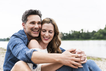 Happy affectionate couple sitting at the riverside - UUF14489