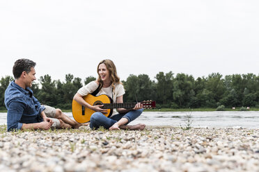 Glückliche Frau mit Mann am Flussufer beim Gitarrenspiel - UUF14490