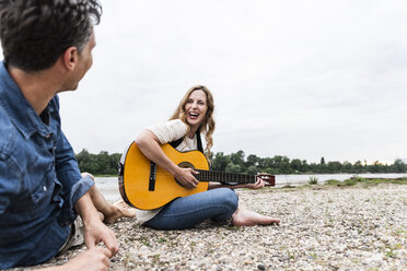 Glückliche Frau mit Mann am Flussufer beim Gitarrenspiel - UUF14491