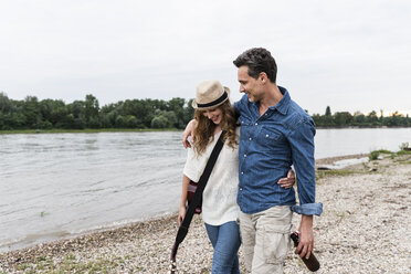 Glückliches Paar, das am Flussufer mit Bierflasche und Gitarre spazieren geht - UUF14493