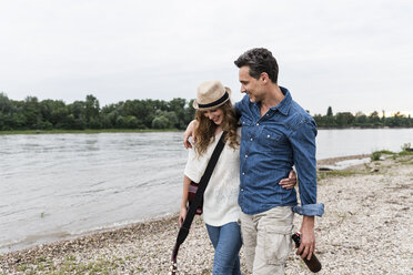 Happy couple walking at the riverside with beer bottle and guitar - UUF14493