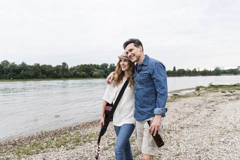 Happy couple walking at the riverside with beer bottle and guitar stock photo