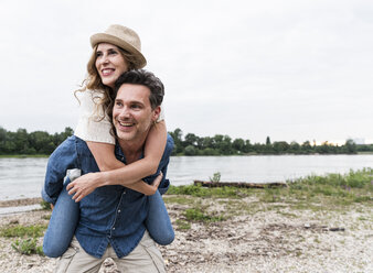 Happy man carrying girlfriend piggyback at the riverside - UUF14497