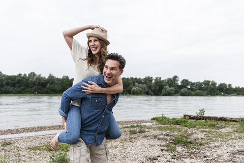 Happy man carrying girlfriend piggyback at the riverside stock photo