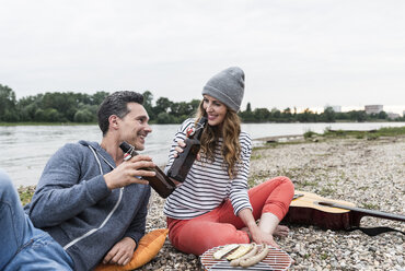 Happy couple relaxing at the riverside clinking beer bottles - UUF14500