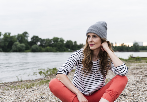 Portrait of woman wearing wooly hat sitting at the riverside stock photo