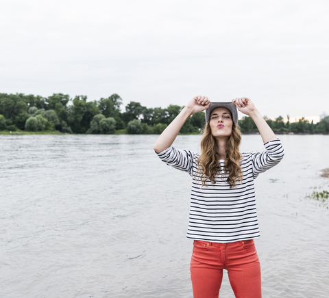 Verspielte Frau mit Wollmütze an einem Fluss, die schmollt, lizenzfreies Stockfoto