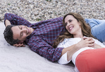 Glückliches, zärtliches Paar auf einer Decke am Kieselstrand liegend - UUF14528