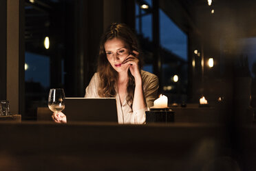 Woman having glass of white wine looking at laptop - UUF14544