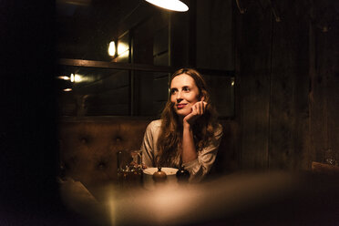 Smiling woman sitting at dining table looking sideways - UUF14551