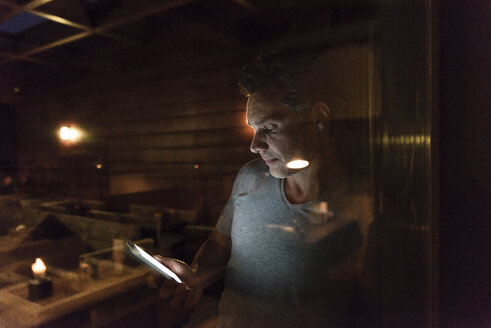 Man leaning at the window in a dark illuminated room using cell phone - UUF14552