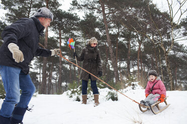 Vater und Großmutter ziehen Mädchen auf Schlitten im Schnee - CUF40441