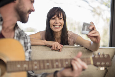 Young man at home playing guitar and woman taking a selfie - ZEF15826