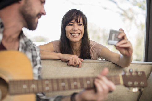 Junger Mann zu Hause spielt Gitarre und Frau nimmt ein Selfie - ZEF15826